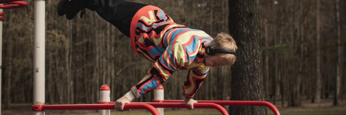 Young man wearing colorful outfit doing calisthenics on red bars in Vilnius park.